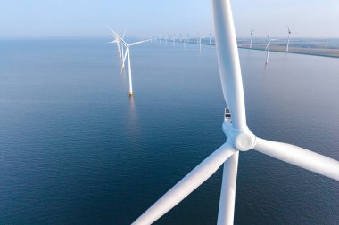 Okyanusta dik duran rüzgar türbinlerinin manzarası Flevoland, Hollanda kıyı şeridi boyunca sürdürülebilir teknoloji ve yenilenebilir enerjinin güzelliğini gözler önüne seriyor..