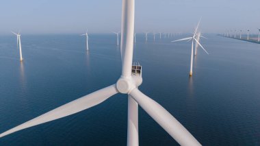 Rüzgar türbinleri, Hollanda 'nın Flevoland kentindeki açık deniz rüzgâr çiftliğinde temiz enerji üreterek mavi denize karşı dik dururlar. Bu manzaralı manzara sürdürülebilirlik ve teknolojiye bağlılığı vurguluyor.