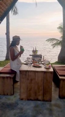 Sahildeki köy masasında otururken hindistan cevizi içeceğiyle nefis bir yemeğin tadını çıkarmak. Güneş sakin okyanusun üzerinde batar, Koh Mak, Tayland 'da mükemmel bir tatil ortamı yaratır..