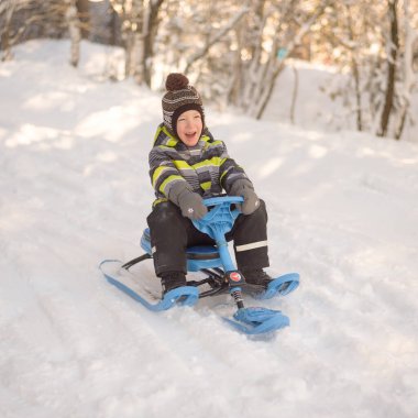 Çocuk tepeden aşağı yuvarlanıyor. Kışın karda oynayan çocuk