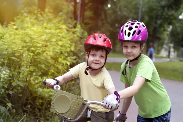 A girl helps a little boy learn to ride a bike. Summer children\'s vacations. Family values of the relationship between brother and sister.