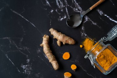 Siyah mermer bir masa ve mutfak gereçleri üzerinde taze zerdeçal yakın çekim. Taze Hint tıbbi baharatı