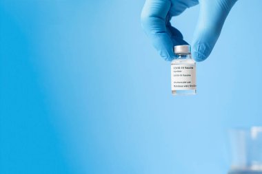 Mavi eldivenli, mavi arka planda Covid 19 aşısı olan bir cam şişe tutuyordu. Uzayı kopyala Sağlık tedavisi kavramı