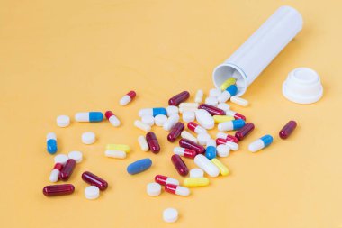 Sarı arka planda şişeden çıkan renkli hapların ön görüntüsü..