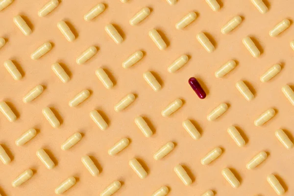 Fashion pattern made with yellow pharmaceutical medicine pills on color pastel orange background. The pattern it is broken with a red pill. Medicine creative concepts. Trendy colors