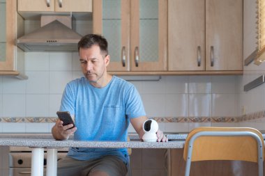 Adam akıllı telefonuyla güvenlik kamerası kurarken mutfakta oturuyordu. Güvenlik ve güvenlik kavramı.