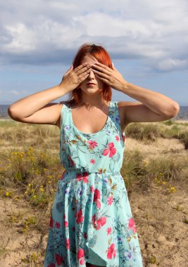 Redhead girl covering her eyes with hands at the seashore clipart