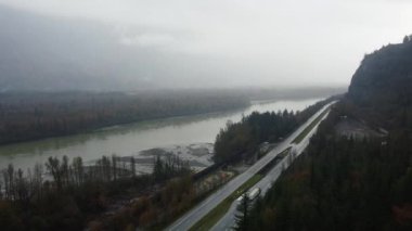 Bulutlu bir günde nehir ve dağ arasındaki otoyolun insansız hava aracı görüntüsü