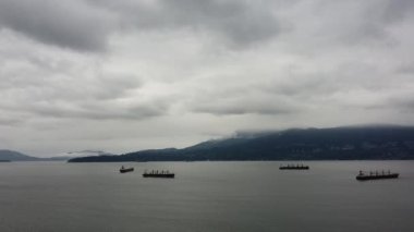 Bulutlu bir günde arka planda dağlarla birlikte koydaki kargo gemisinin hava görüntüsü.