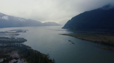 Sis kaplı yüksek dağlarla çevrili nehir koylarının üzerinden uçuyorlar.