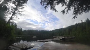 Hareket eden bulutlar, temiz göl üzerinde zaman kaybıdır. Kırık rıhtımla çevrili bir orman vardır.