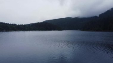 Fly over the lake surrounded by green mountains on a cloudy day in Canada