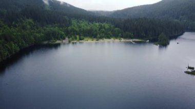 Aerial view of empty beach near lake surrounded with spruce hills on a rainy day