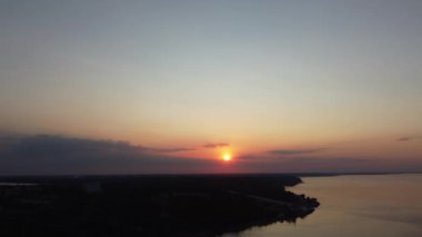 Parlak turuncu güneşe doğru uçuyor denizin üzerinde ve koyu yeşil kıyı tepelerinde