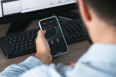 Borsa telefonu elinde ve masaüstü bilgisayarı yeşil ve kırmızı çizelgeler
