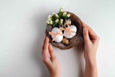 Paskalya yumurtaları ve çiçekleri beyaz arka planda tutan genç bir kadın. Tebrik kartı