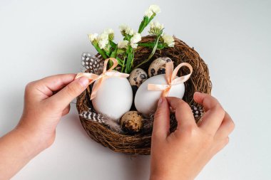 Paskalya yumurtalarını ve çiçekleri beyaz arka planda tutan çocuk. Tebrik kartı