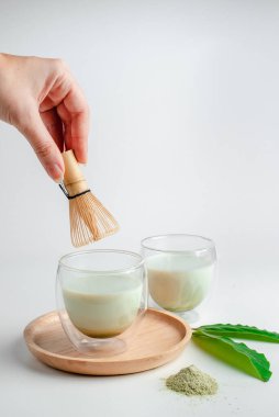 Genç kadın elinde çay çırpmak için çırpıcıyı tutuyor. Çay seremonisi. Matcha yeşil çay tozu. Organik yeşil çay yaprağı, beyaz arka planda izole edilmiş, organik ürün, gelenek açısından sağlıklı.