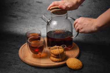 Genç bayan çay dolduruyor. Nefis bir kahvaltı. Yulaf kurabiyesi. Sabah vakti çay saatidir. Mutfakta çay yapan bir kadın. Kapatın. Bir fincana siyah çay dolduran cam çaydanlık.