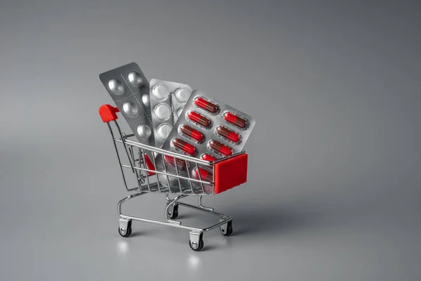 Tablets in shopping basket. Red pills on a pink background. Pills and capsules in shopping cart close-up. oncept of buying medicines online, delivery of medicines during an epidemic.