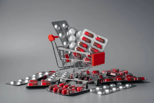 Tablets in shopping basket. Red pills on a pink background. Pills and capsules in shopping cart close-up. oncept of buying medicines online, delivery of medicines during an epidemic.