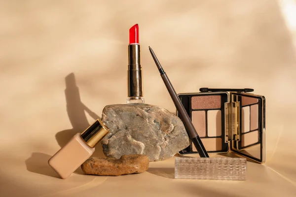 Makeup cosmetics in beige tones. Red lipstick, eye shadow, eyebrow pencil, foundation. The shadow of a plant on a beige background. Trendy cosmetics .
