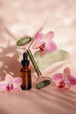 Spa salonu için fotoğraf. Yüz masajı için paten ve Guasha kazıyıcısı, masaj yağı, siyah sıcak spa taşları, pembe orkideler, pembe arka planda beyaz havlu. Denge ve yükselme trend biçimi