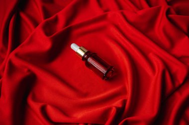 Kırmızı bir bezin üzerinde kırmızı bir şişenin içindeki yüz için esans. Kumaşın kıvrımları çok güzel. Yüz bakımı için yağ. Masaj spa losyonu