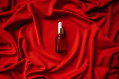 Kırmızı bir bezin üzerinde kırmızı bir şişenin içindeki yüz için esans. Kumaşın kıvrımları çok güzel. Yüz bakımı için yağ. Masaj spa losyonu