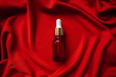 Kırmızı bir bezin üzerinde kırmızı bir şişenin içindeki yüz için esans. Kumaşın kıvrımları çok güzel. Yüz bakımı için yağ. Masaj spa losyonu