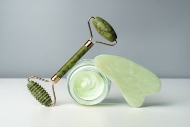 Yüz kremi ve yeşim masaj silindiri. Sağlıklı ve genç cilt için kaldırma. Siyah arka planda organik kozmetik ürünler. Cilt bakımı moda. Yüz ve boyun masajı için Gouache kazıyıcı