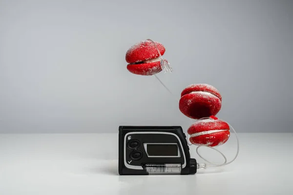 Insulin pump and red macaroon cakes on a gray background. Trending style levitation. Diabetes and sugary foods. Increased blood glucose. Insulin pen for diabetics