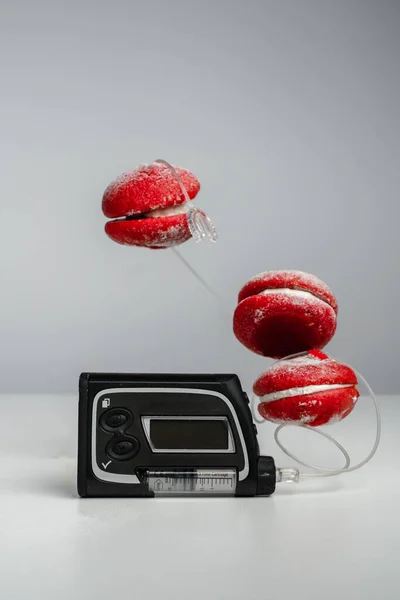 Insulin pump and red macaroon cakes on a gray background. Trending style levitation. Diabetes and sugary foods. Increased blood glucose. Insulin pen for diabetics