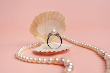 Lüks aksesuarlar. Pembe arka planda inci kabuklu bir yüzük. İnci kolye. Düğün hediyesi olarak. Nişan yüzüğü.