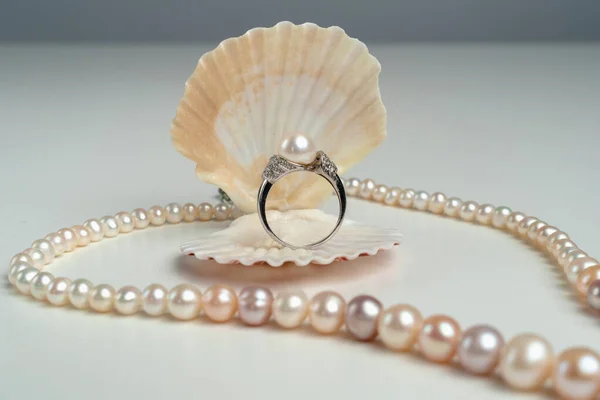 Luxury accessories. Ring with pearls in a shell on a pink background. Pearl necklace. Present for the wedding. Engagement ring