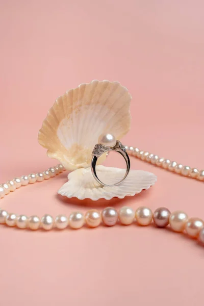 Luxury accessories. Ring with pearls in a shell on a pink background. Pearl necklace. Present for the wedding. Engagement ring