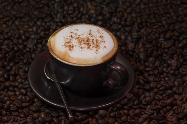 Капучино кава над смаженими кавовими зернами як фон — стокове фото