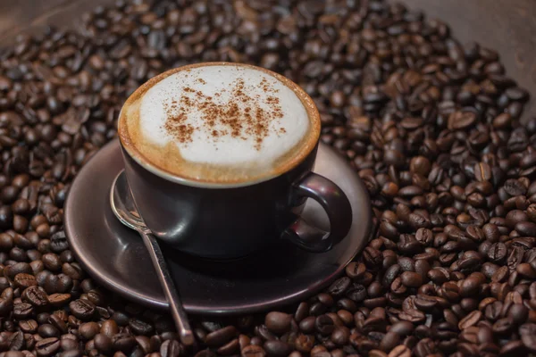 Café capuchino sobre granos de café tostados como fondo —  Fotos de Stock