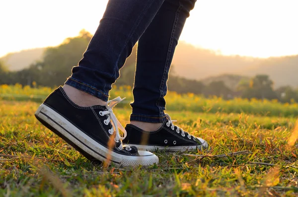 Frau trägt Turnschuhe, wenn sie durch eine Wiese mit üppigem Gras geht — Stockfoto