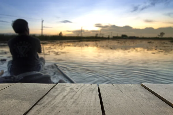 Desenfoque y desenfoque imagen de madera terraza y hombre solitario sentado en el barco en el hermoso lago cerca de casa para el uso de fondo — Foto de Stock