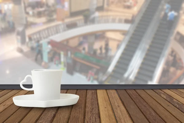 Coffee cup on wood table with fade out of shopping mall as backg — Stock Photo, Image
