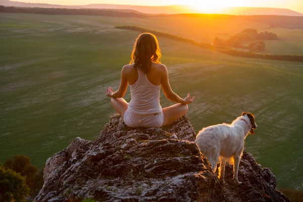 Mujer joven está practicando yogaon una roca en la puesta del sol — Foto de Stock