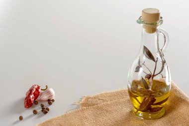 Çuvalın üzerinde duran cam sürahide zeytin yağı ve zeytin filizi. Yanında da acı kırmızı biber, sarımsak ve baharat. Beyaz arka plan. Mesajın için yer aç. Yakın plan.. 