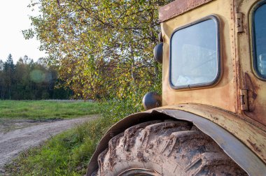 Taksinin bir parçası ve eski sarı bir traktörün tekerlekleri tarla yolu ve ormanın arka planında. Güneşli bir gün. Seçici odaklanma. Uzayı kopyala Kapat..