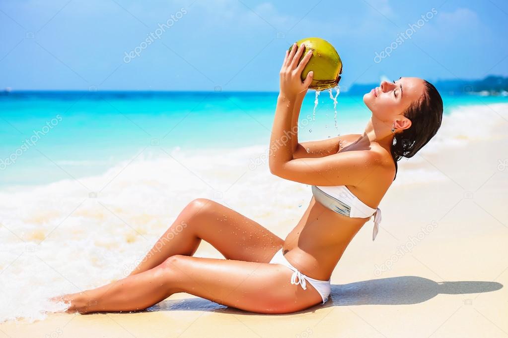 Beautiful young woman drinking coconut water on a white sand tropical beach