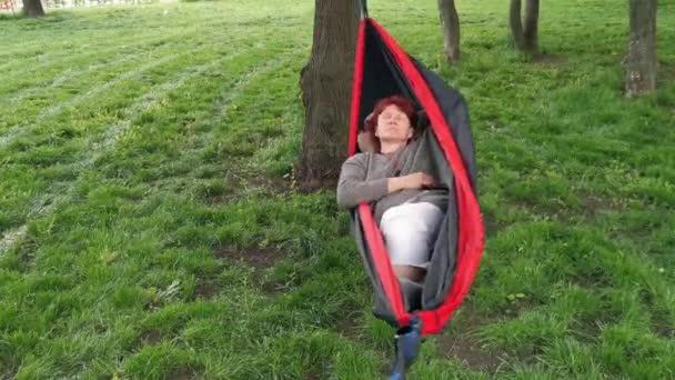 公園の女性はハンモックで休んでいて スマートフォンを見ています — ストック動画