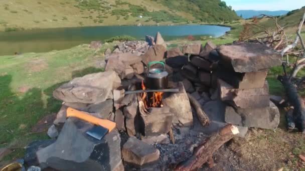 Hervidor de agua para acampar en un incendio cerca de un lago de montaña. — Vídeos de Stock