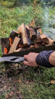 Mangalda odun yakarken çekilmiş dikey bir video. Adam dışarıda şömine demiri kullanarak yemek ve ısıtma için alevleri yakıyor.