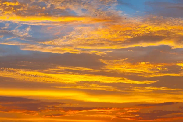 Vibrant sunset or sunrise sky featuring dramatic gold and orange clouds. Beautiful nature landscape background, conveying peace and tranquility.