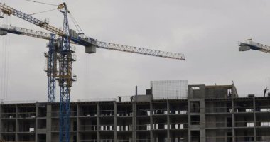 Ağır inşaat vinçleri, sanayi gelişimini ve büyümesini gösteren bulutlu bir gökyüzünün altında kentsel bir inşaat sahasına yeni bir yerleşim yeri inşa ediyor.